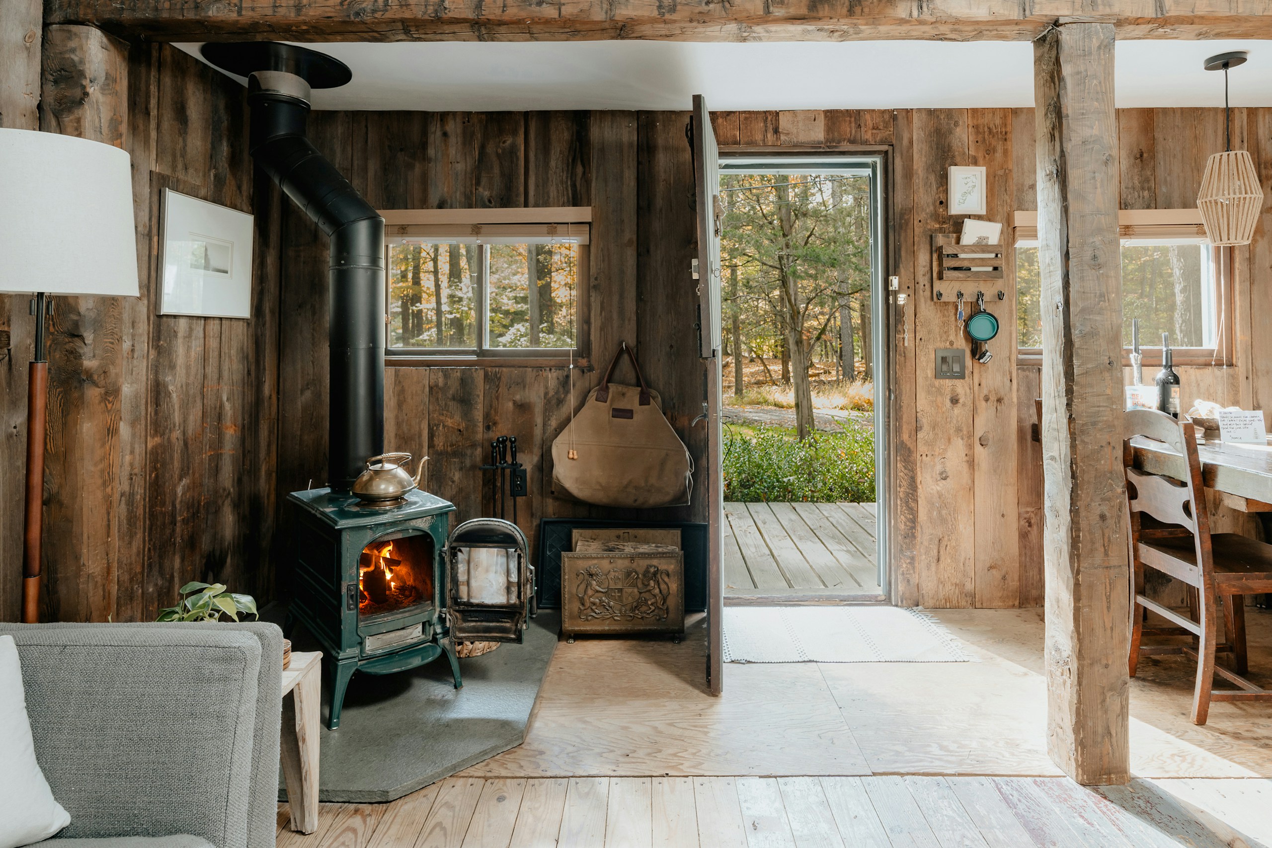 Cabin interior with a wood stove and forest beyond